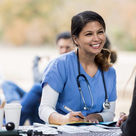 Smiling mid adult nurse listens as a female patient discusses her symptoms. The patient is visiting a free clinic.