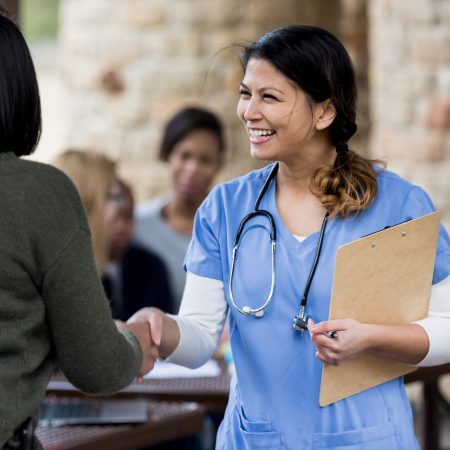 The female mid adult doctor stands to shake hands with an unrecognizable female patient at the free health clinic.