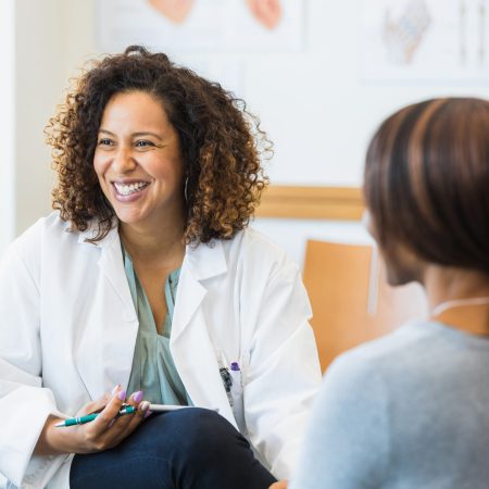 A mid adult female healthcare worker and her unrecognizable female colleague smile at an unseen person during their weekly meeting.